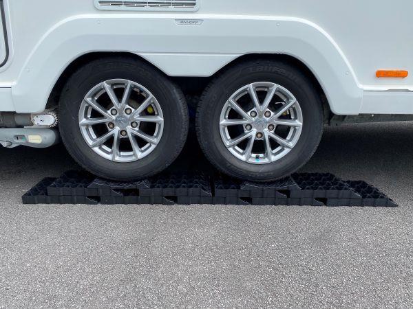 A set of black Milenco Twin Axle Stacka Level Set blocks placed under the front wheels of a white caravan to level it.