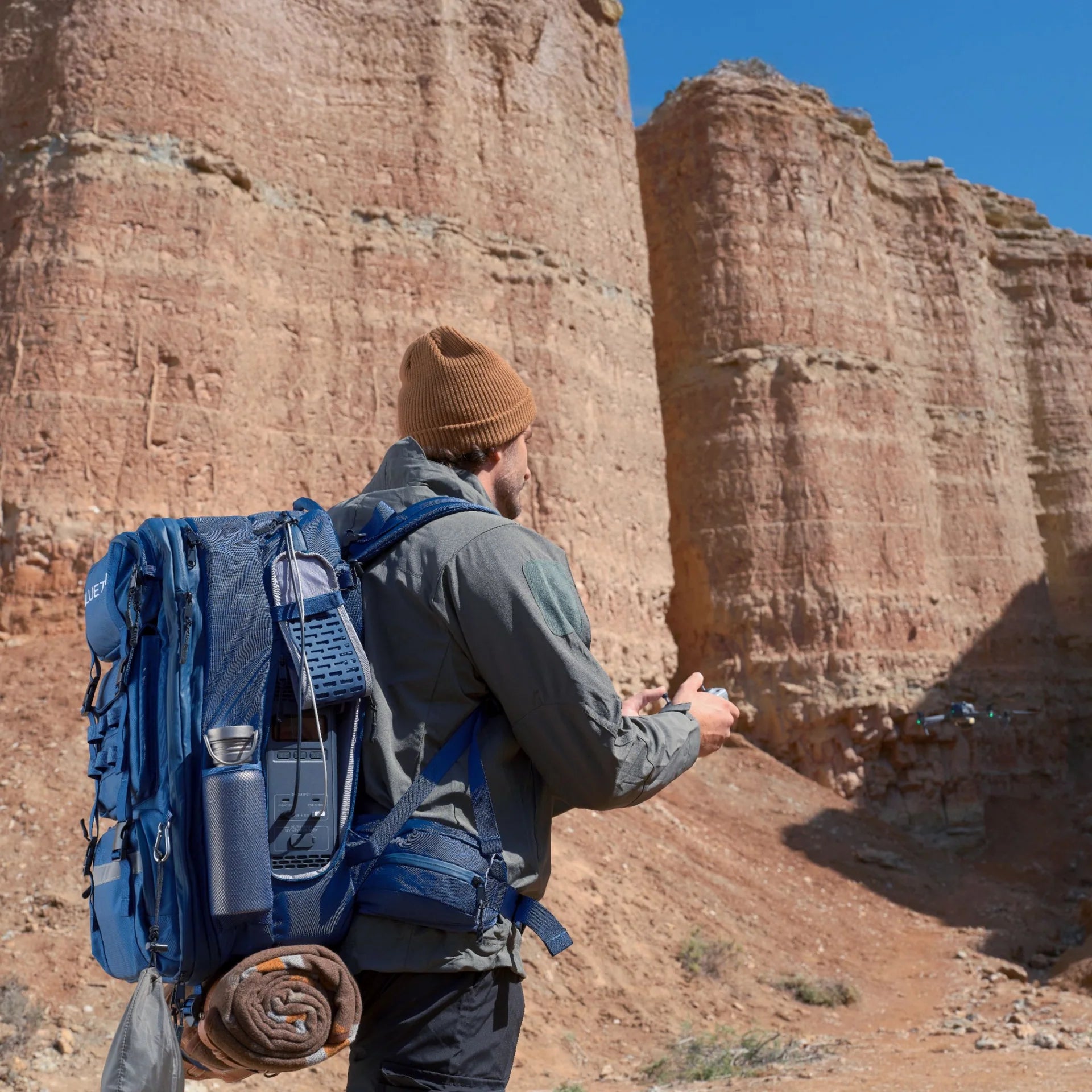 Person with a blue backpack in a desert landscape with rock formations.