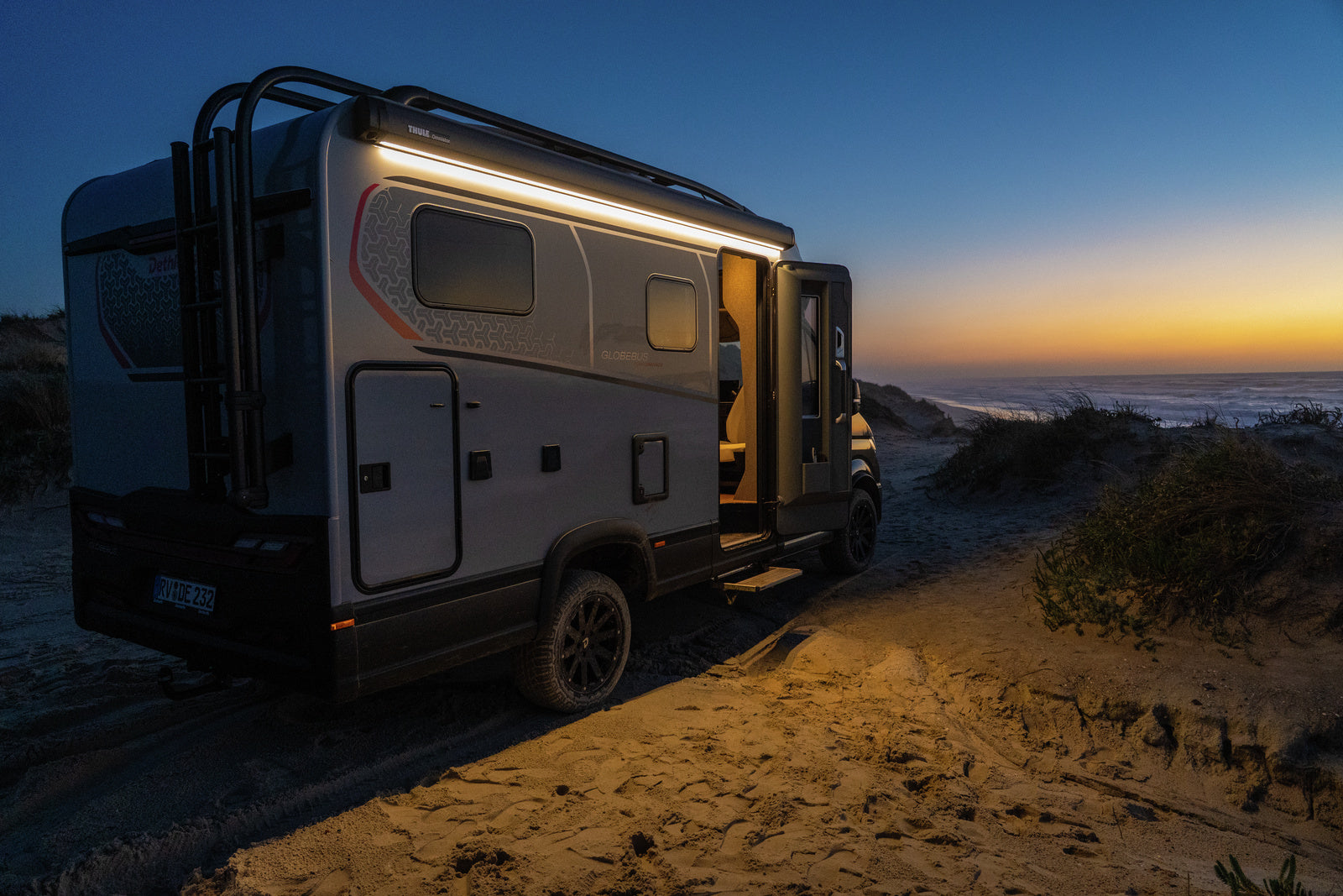 Camper van parked on a sandy beach at sunset